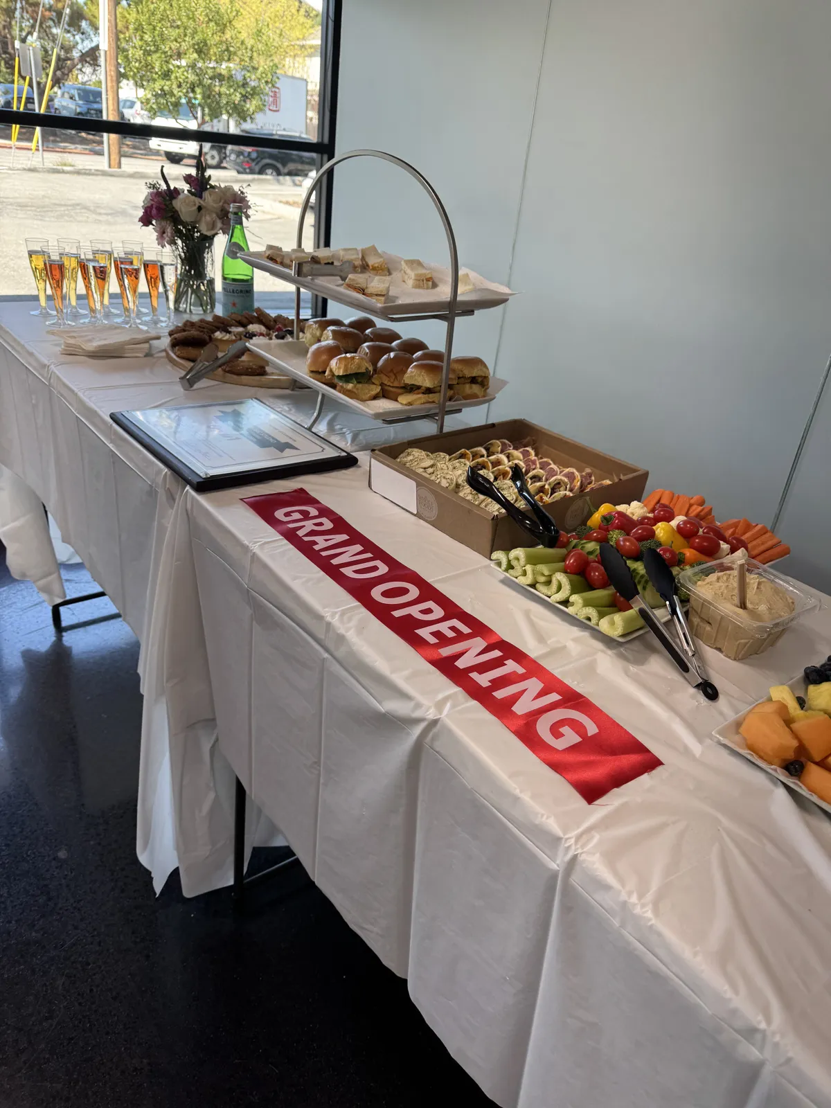 Grand opening reception table inside the Opus 1 Music Studio Palo Alto campus, with sparkling drinks, flowers, and refreshments beside the red grand opening ribbon.